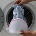 Mains plaçant des vêtements dans un sachet de lavage blanc en maille avec fermeture éclair rose dans une machine à laver.