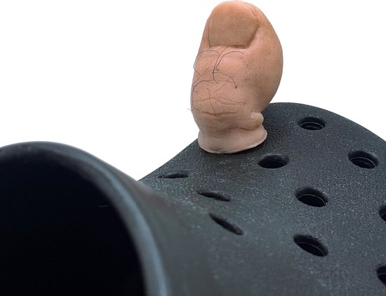 Une breloque d'orteil rose avec des poils noirs, assise sur une chaussure Crocs noire.