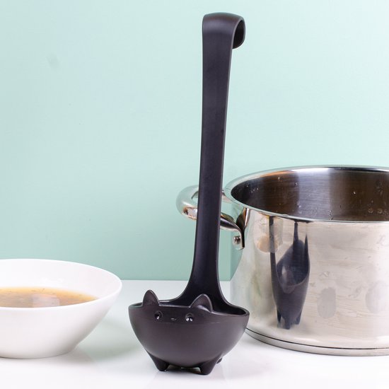 Zwarte soeplepel in de vorm van een katje met pootjes, naast een pan soep en een kookpot.