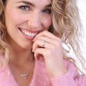Een lachende blonde vrouw met krullen, met haar hand bij haar gezicht en draagt een zilverkleurige ring.