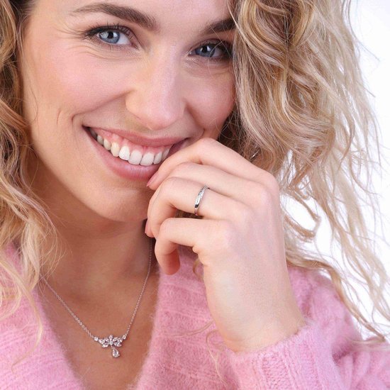 Een lachende blonde vrouw met krullen, met haar hand bij haar gezicht en draagt een zilverkleurige ring.