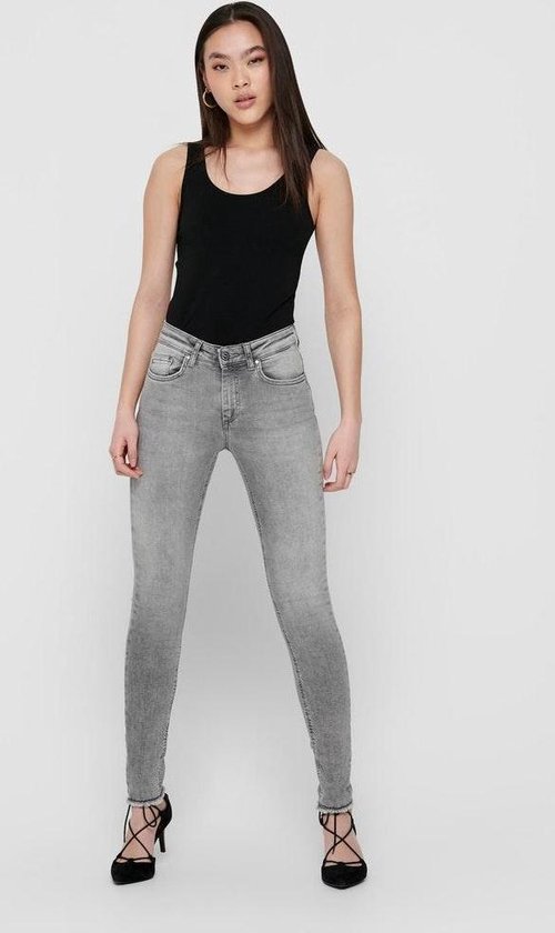 Model in zwarte tanktop en grijze skinny jeans, met hoge hakken.