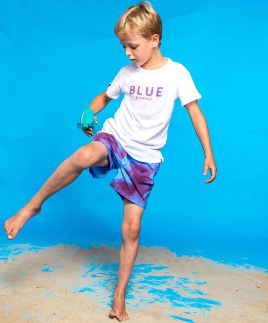 Jongetje met witte T-shirt met tekst 'BLUE BY SEASONS', draagt een paarsblauwe zwembroek met tie-dye patroon.