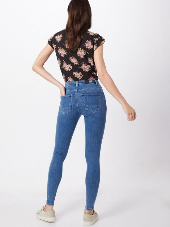 Model in een zwarte top met bloemenprint en lichtblauwe skinny jeans. Sneakers. Achteraanzicht.