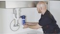 Man installeert een witte en blauwe boiler onder een gootsteen.