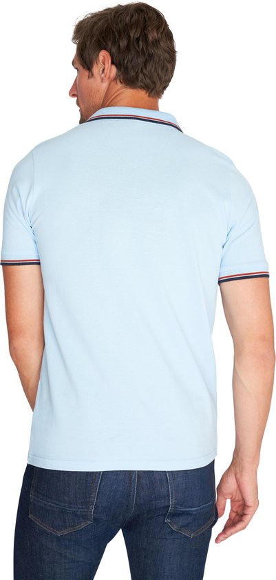 Achterkant van een man in lichtblauw poloshirt met marineblauwe en rode strepen op de kraag en mouwen, met jeans.