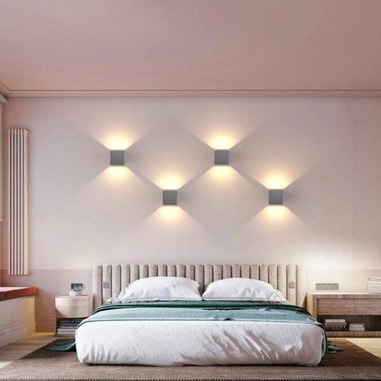 Slaapkamer met een bed en vier grijze kubuswandlampen aan de muur die een zacht licht geven.
