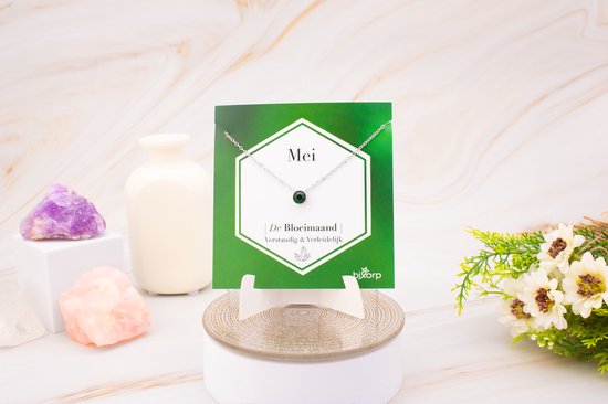 Zilverkleurige ketting met groene zirkonia hanger op een groene kaart met 'Mei De Bloemmaand' erop, naast decoratie.