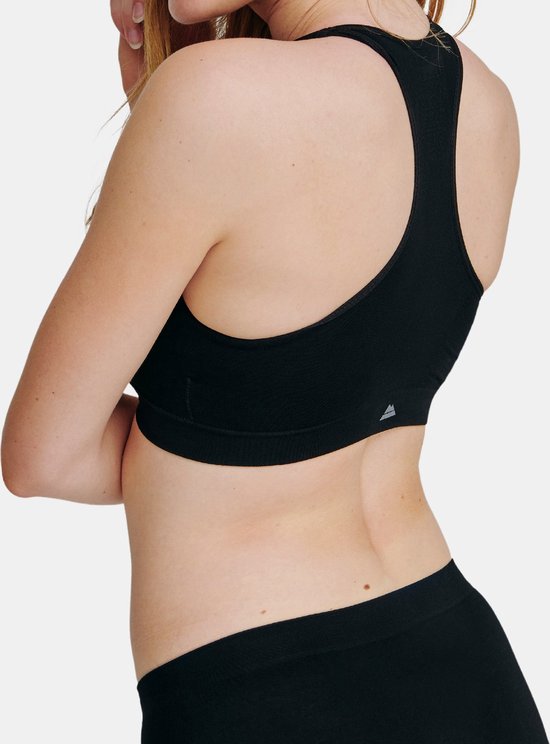 Zij-aanzicht van model dat een zwarte bralette en slip draagt. Grijze achtergrond.