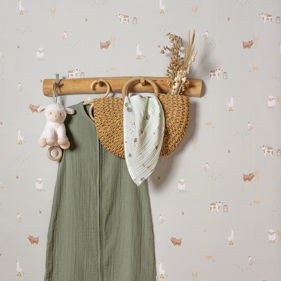 Kinderkamer met 'Little Farm' behang, een groene slaapzak, rieten mand en schapenknuffel aan een kapstok.