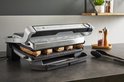 Zilverkleurige Tefal OptiGrill+ XL contactgrill met zes stukken vlees die grillen op de geribbelde platen. De grill heeft een RVS-look en een indicatorlicht.