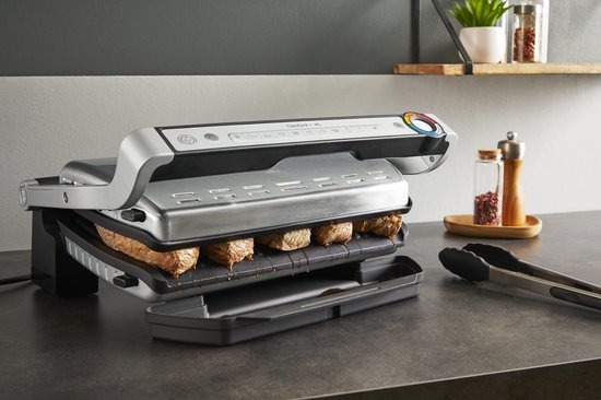 Zilverkleurige Tefal OptiGrill+ XL contactgrill met zes stukken vlees die grillen op de geribbelde platen. De grill heeft een RVS-look en een indicatorlicht.