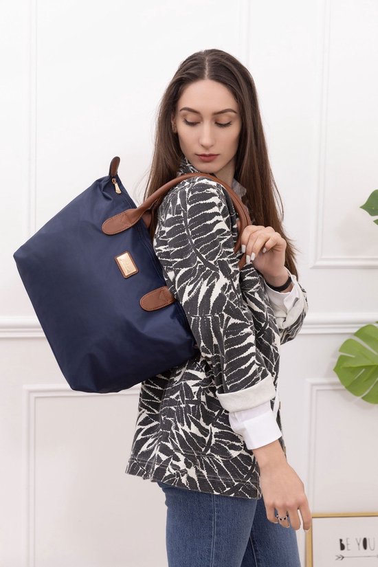 Sac en nylon bleu foncé avec anses en cuir marron, porté sur l'épaule par une femme portant une veste noir et blanc.