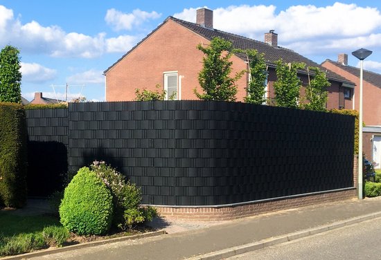 Een zwart, modulair hekwerk met bakstenen voet en groene struiken op de voorgrond, voor een bakstenen woning.
