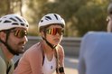 Twee fietsers, een vrouw met een roze jack en een man met een groen jack, dragen sportbrillen met gespiegelde lenzen.