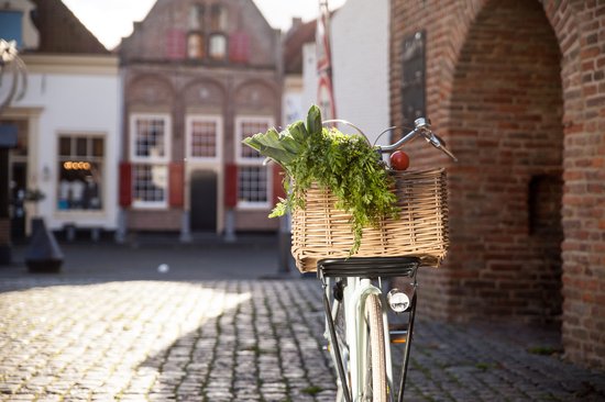 Fiets met een rieten mand gevuld met groente op een geplaveide straat.
