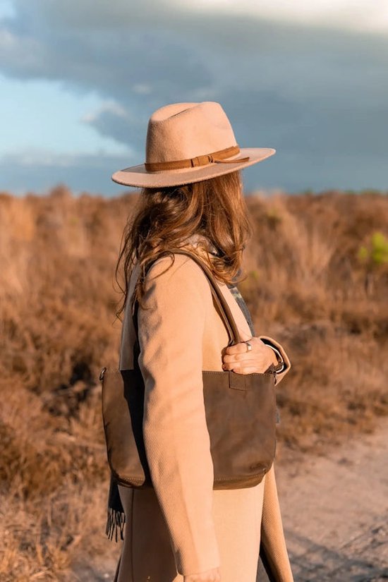 Femme portant un manteau beige et un chapeau, porte un sac en cuir marron foncé.