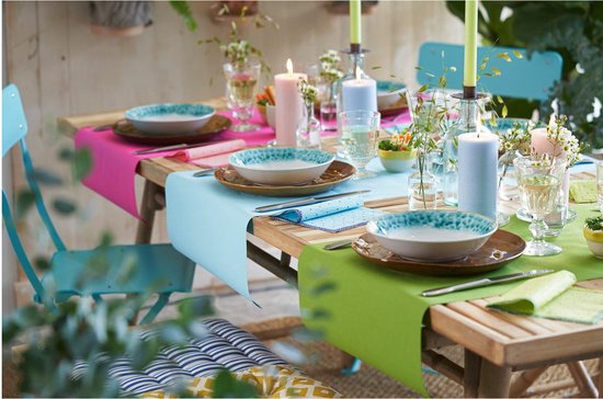 Een gedekte tafel met turquoise, roze en groene lopers, gedekt met borden, glazen en kaarsen.