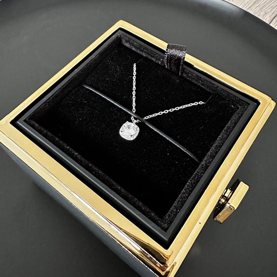 Zilveren ketting met glinsterende hanger in zwarte juwelendoos met gouden rand.