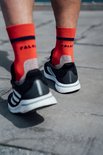Pieds d'un coureur portant des chaussettes Falke orange vif et des chaussures Adidas noires, courant sur une surface pavée.