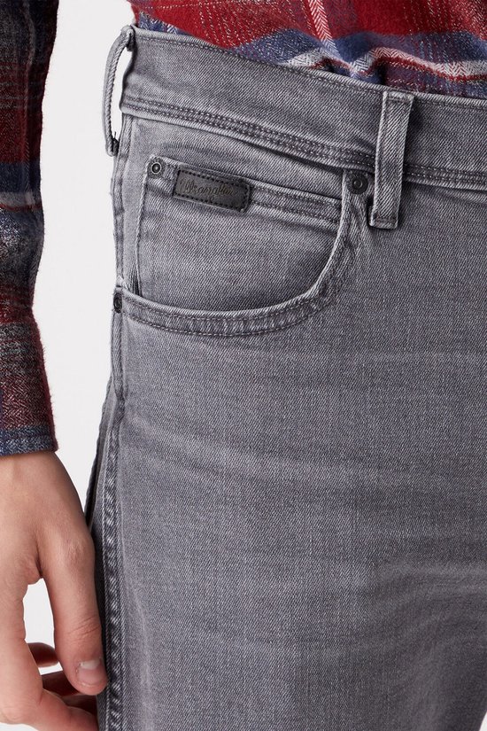 Detail van de voorzak van een donkergrijze straight-fit jeans met een zwarte Wrangler-logopatch.