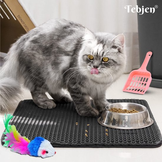 Zwarte kattenbakmat met honingraatpatroon, naast een voerbak met brokjes en kattenspeeltje.