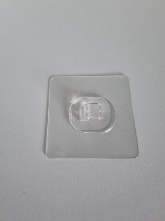 Een enkel transparant kleefhaakje met clip, bevestigd aan een witte muur.