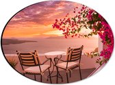 Dibond Ovaal - Tafel met Stoeljes op Balkon met Roze Bloemenstruik met Uitzicht op Zee - 28x21 cm Foto op Ovaal (Met Ophangsysteem)