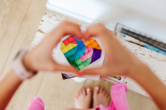 Kinderhanden vormen een hart met transparante, veelkleurige legpuzzelstukken die een hart vormen.