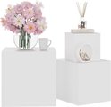 Drie witte kubussen van verschillende groottes, op de middelste staat een boek met diffuser en op de grootste staat een vaas met bloemen en een mok.