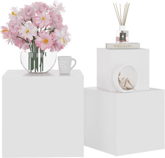 Drie witte kubussen van verschillende groottes, op de middelste staat een boek met diffuser en op de grootste staat een vaas met bloemen en een mok.