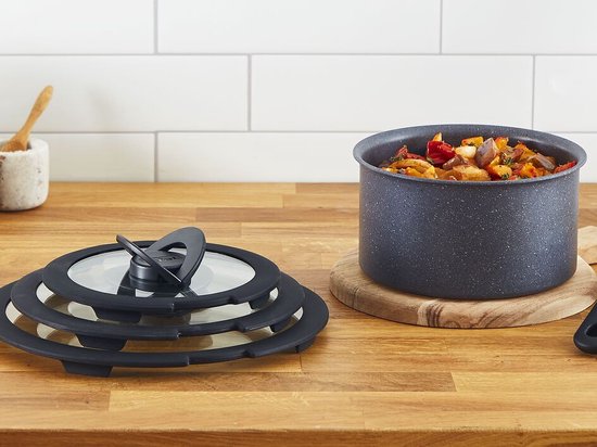 Glazen deksel met zwarte rand en handvat naast een pan met deksel op houten aanrecht.
