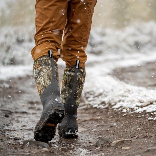 Persoon draagt camouflage Muck Boot laarzen in de sneeuw met een bruine broek.