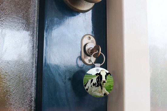 Ronde sleutelhanger met een zwart-witte koe in een weiland, aan een sleutel in een deurkozijn.