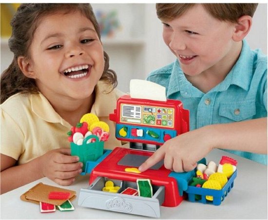 Een lachend meisje houdt een groene boodschappentas vol Play-Doh eten vast bij een rode en blauwe speelgoedkassa.