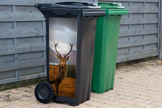 Zwarte kliko met een sticker van een hert, naast een groene kliko bij een houten schutting.