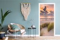 Deursticker met zonsondergang, strand en duingras, in een kamer met blauwe muur.