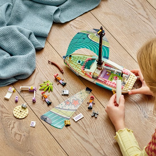 LEGO Friends zeilboot in onderdelen, met poppetjes en accessoires op een houten vloer.