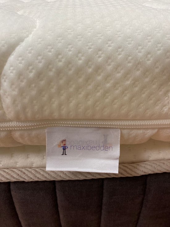 Witte topper matras met label 'maxibedden' en een poppetje. Het label is genaaid aan de zijkant van de matras.