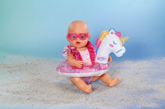 Zittende baby pop met hartjes zonnebril, glitter zwemband met eenhoorn en een glitter zwempak.