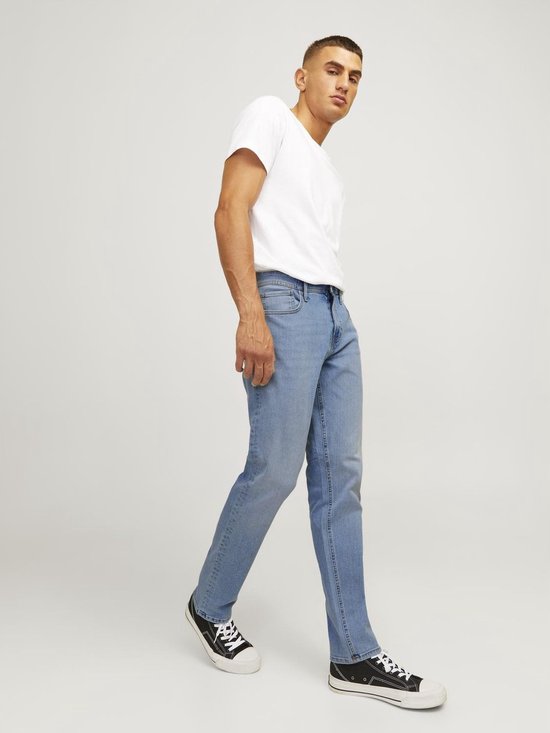 Man poseert in lichtblauwe jeans en wit T-shirt, in een loop.