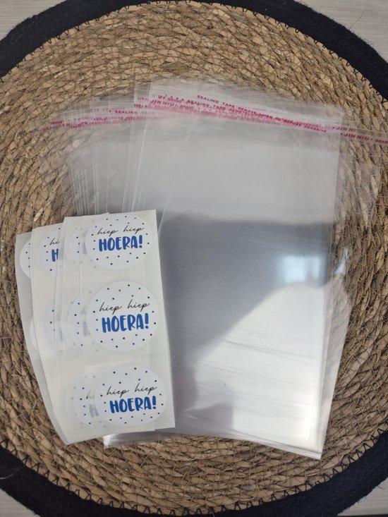 Transparante celofaan zakjes met rode plakrand, met een rol witte stickers met blauwe 'hiep hiep HOERA!' tekst en blauwe stipjes.
