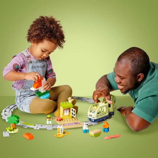 Un enfant et un père jouent avec un train et des rails LEGO Duplo vert clair et accessoires.