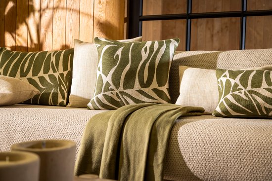 Detail van een beige bank met groene kussens met bladmotief en een plaid.