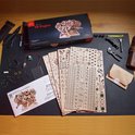 Ugears V8 Engine modelbouwset op een zwarte mat, met de doos, handleiding en alle onderdelen.
