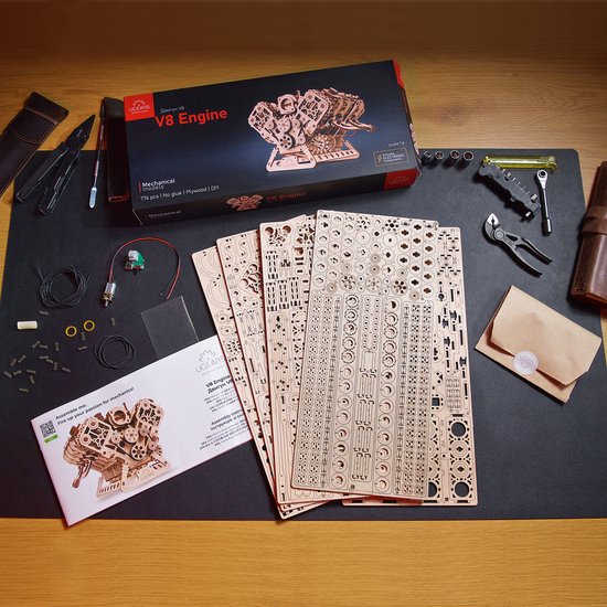 Ugears V8 Engine modelbouwset op een zwarte mat, met de doos, handleiding en alle onderdelen.