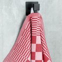Rood-wit geblokt keukendoek hangt aan een zwarte haak aan een grijze muur.