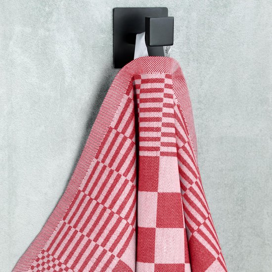 Rood-wit geblokt keukendoek hangt aan een zwarte haak aan een grijze muur.