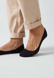 Zwarte onzichtbare sokken van een vrouw met beige broek.