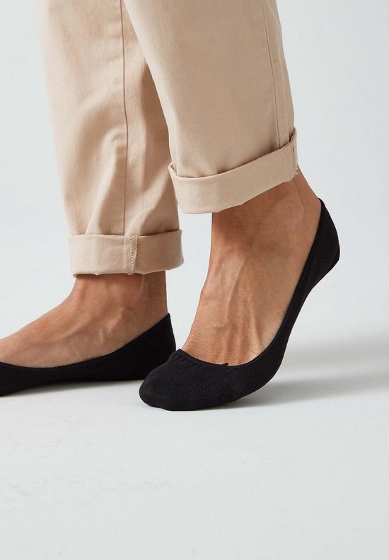 Zwarte onzichtbare sokken van een vrouw met beige broek.